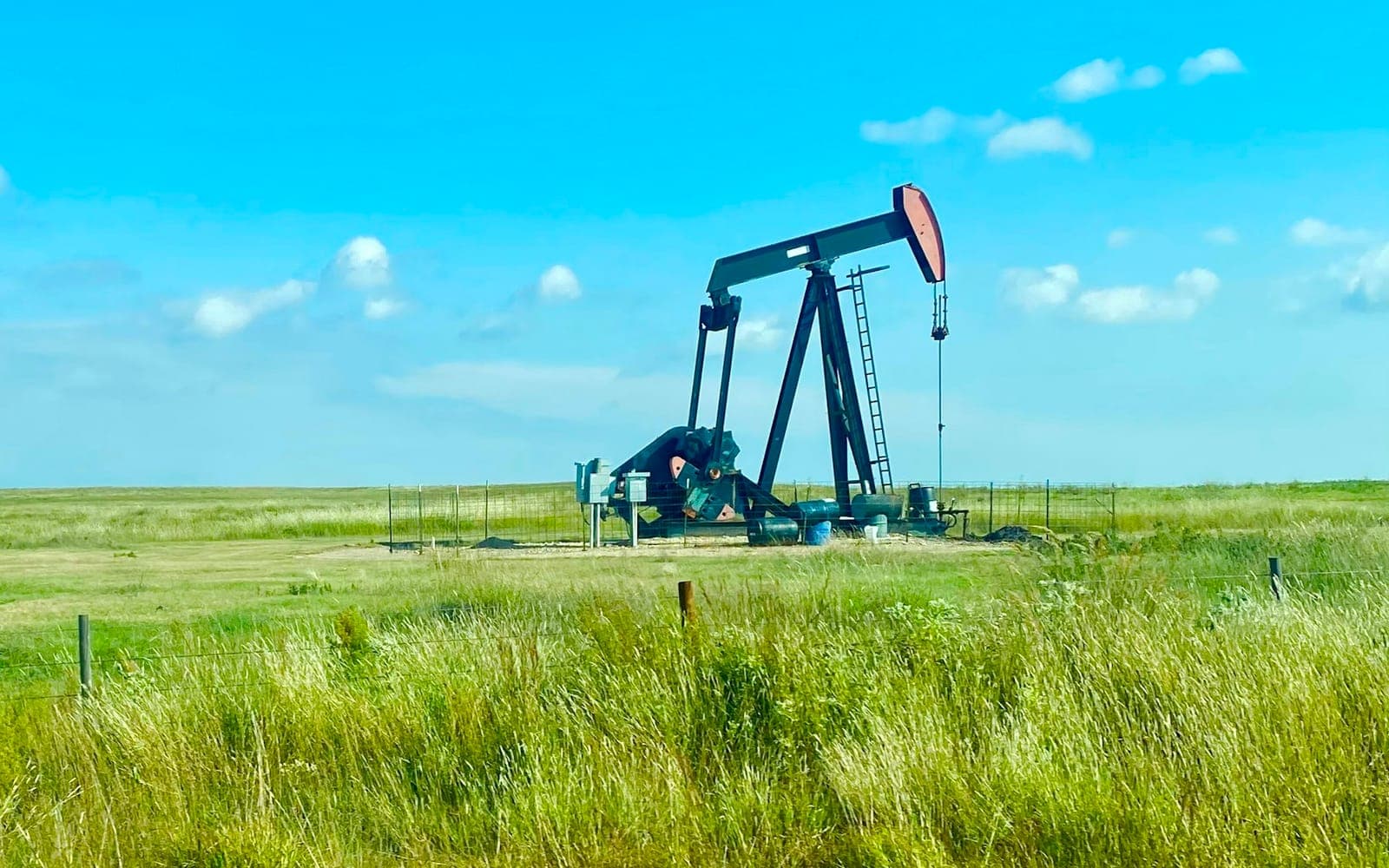 Oil pump jack operating in an open petroleum field under blue sky